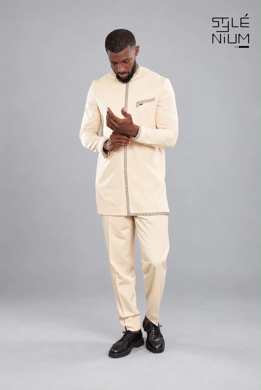 Homme portant en pied un ensemble tunique et pantalon beige bordé de galons à motifs, création AMG STYLENIUM