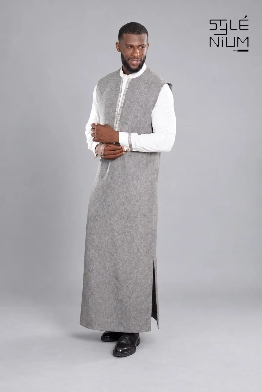 Homme portant un long boubou gris chiné sans manches, fendu sur le côté, par-dessus une tunique blanche à broderies, création AMG STYLENIUM