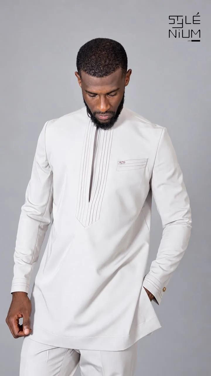 Homme portant une tunique gris clair avec plastron en V à nervures surpiquées et poche poitrine siglée AMG, création AMG STYLENIUM