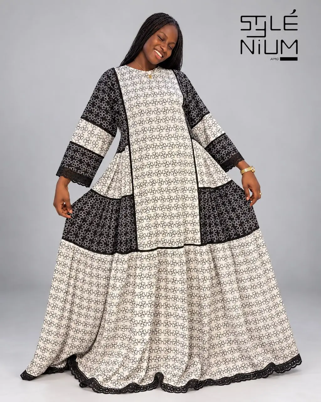 Femme portant une robe longue et ample à empiècements imprimés fleurs noir et blanc, bordée de dentelle noire aux manches et à l'ourlet, création AMG STYLENIUM
